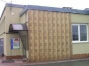 Budynek firmy z Jeleniej Góry z charakterystyczną, pionową okładziną elewacyjną w odcieniach beżu i brązu, widoczne wejście z daszkiem i tablicą informacyjną.