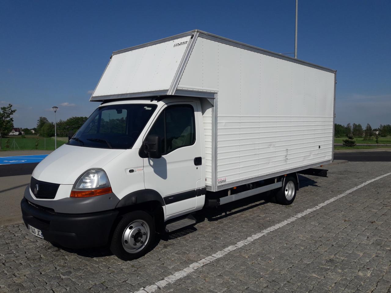 Biały Renault Master z zabudową kontenerową, zaparkowany na brukowanym placu w słoneczny dzień. Widoczne detale: czarne zderzaki, relingi dachowe, tablica rejestracyjna.