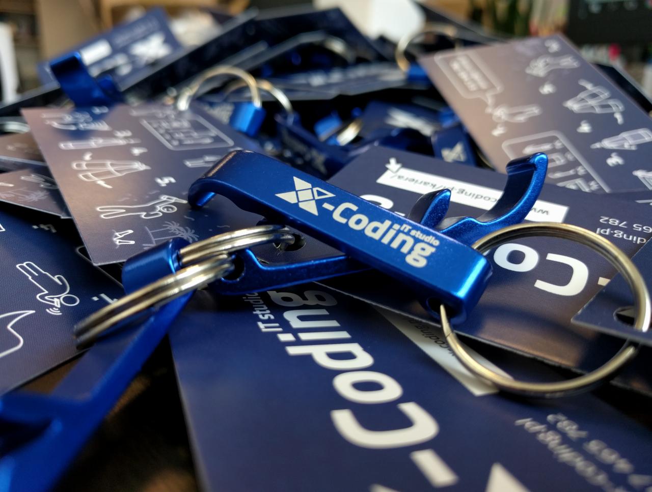 Stos niebieskich breloków z otwieraczem do butelek i logo 'X-Coding IT studio' oraz wizytówek z grafikami przedstawiającymi proces rekrutacji, leżących na sobie.