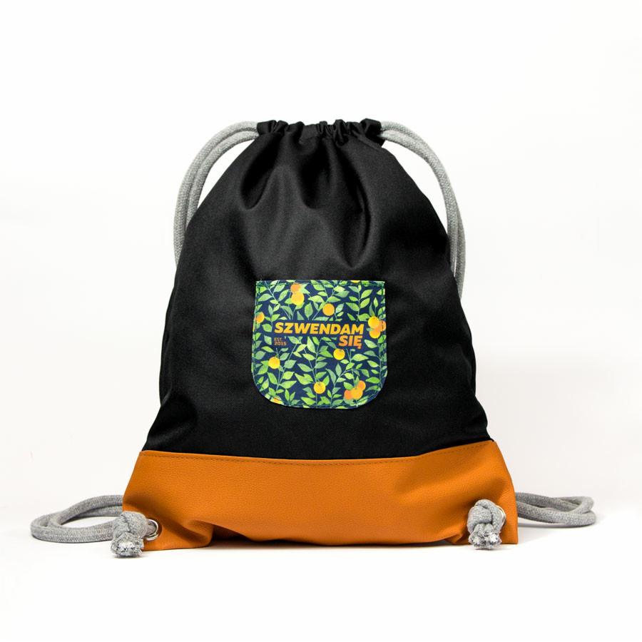 Czarno-pomarańczowy worek ze sznurkami i kieszonką w pomarańcze z napisem 'SZWENDAM SIĘ' na białym tle.