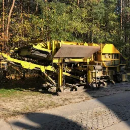 Żółta maszyna do robót ziemnych stoi na betonowej powierzchni, otoczona jesiennym lasem.