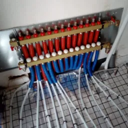 Rozdzielacz ogrzewania podłogowego z rurami w kolorach czerwonym i niebieskim, ułożonymi na folii z rastrem, widok z góry.