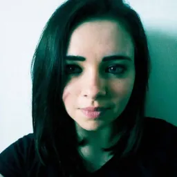 Portret młodej kobiety z ciemnymi włosami i jasnymi oczami, ujęcie z bliska na tle jasnej ściany, oświetlenie z lewej strony.