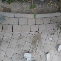 Układanie szarej kostki brukowej w łuk, widoczne niedociągnięcia i resztki materiału, but roboczy w lewym górnym rogu.