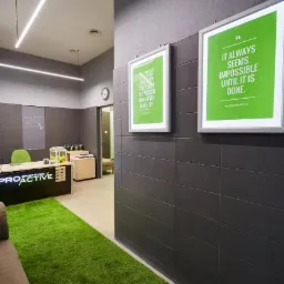 Wnętrze gabinetu z recepcją, zielonym dywanem imitującym trawę i motywującymi plakatami na ścianach w odcieniach szarości.