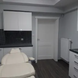 Jasny fotel kosmetyczny w minimalistycznym gabinecie z ciemną mozaiką nad blatem i drewnopodobną podłogą