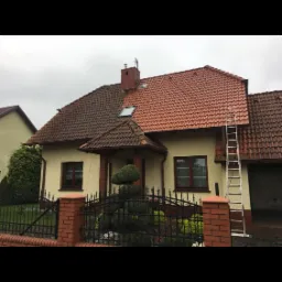 Dom jednorodzinny z dachem w połowie wyczyszczonym, widoczna różnica w kolorze dachówek przed i po, drabina oparta o ścianę, pochmurne niebo.