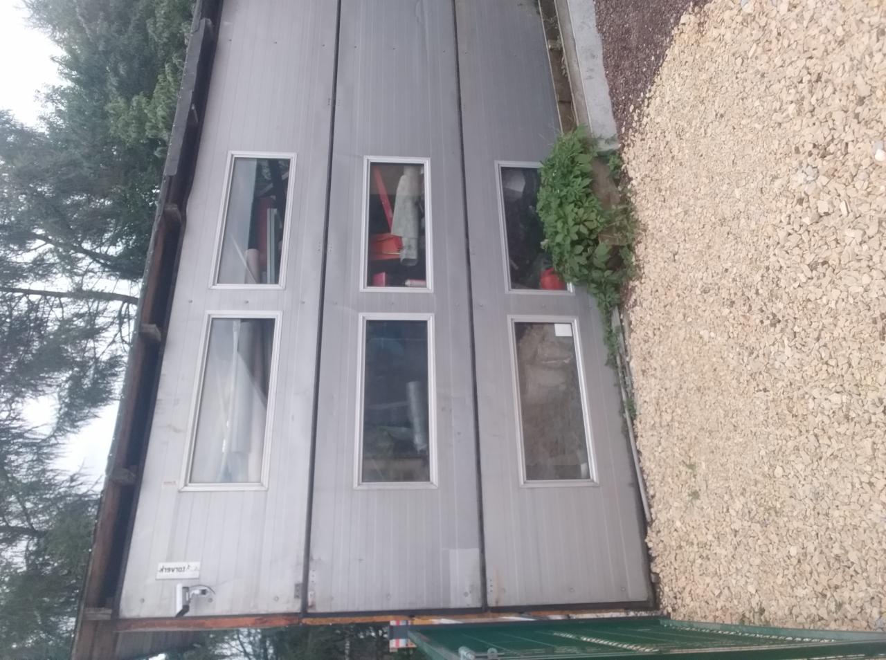Metalowy garaż z sześcioma oknami, obok widoczne kamienie i zieleń, ujęcie z dołu pod kątem.