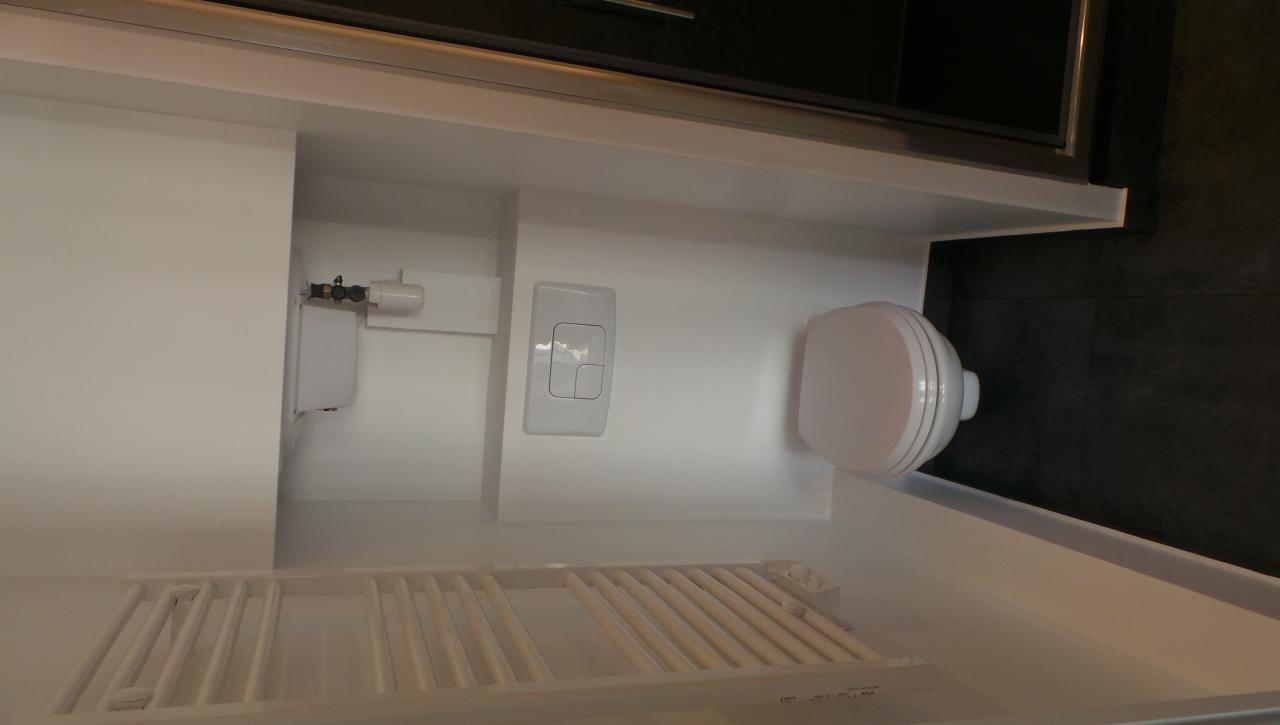 Nowoczesna, minimalistyczna łazienka z podwieszaną toaletą, grzejnikiem drabinkowym i czarnymi płytkami na ścianie, widoczne elementy instalacji.