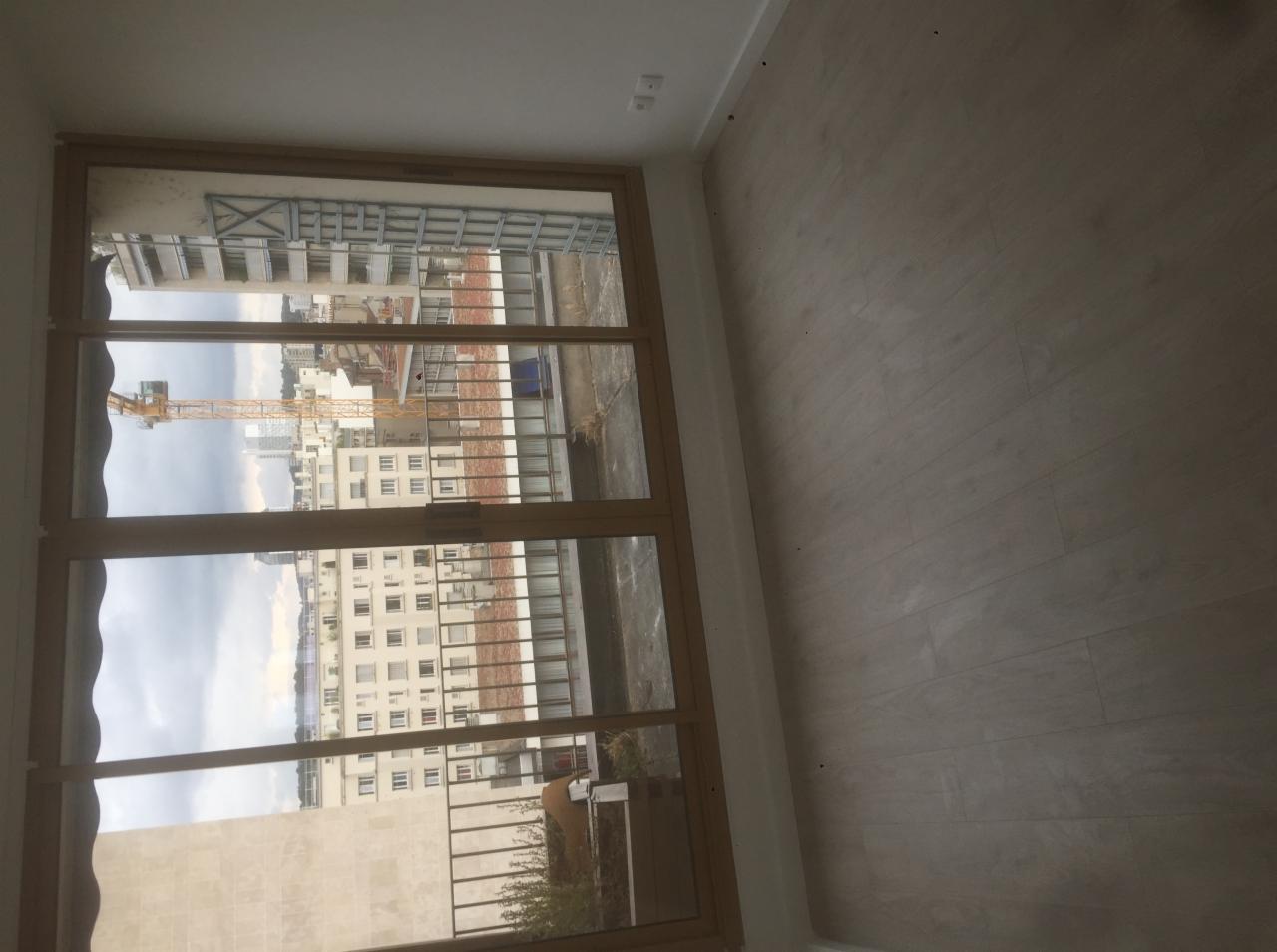 Wnętrze pokoju w Chomranicach z dużym oknem z widokiem na budowę i miasto, świeżo położona podłoga, ściany przygotowane do malowania.