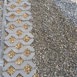 Szara ażurowa nawierzchnia z betonu wypełniona drobnym żwirem, obok wysypana szarym grysem.