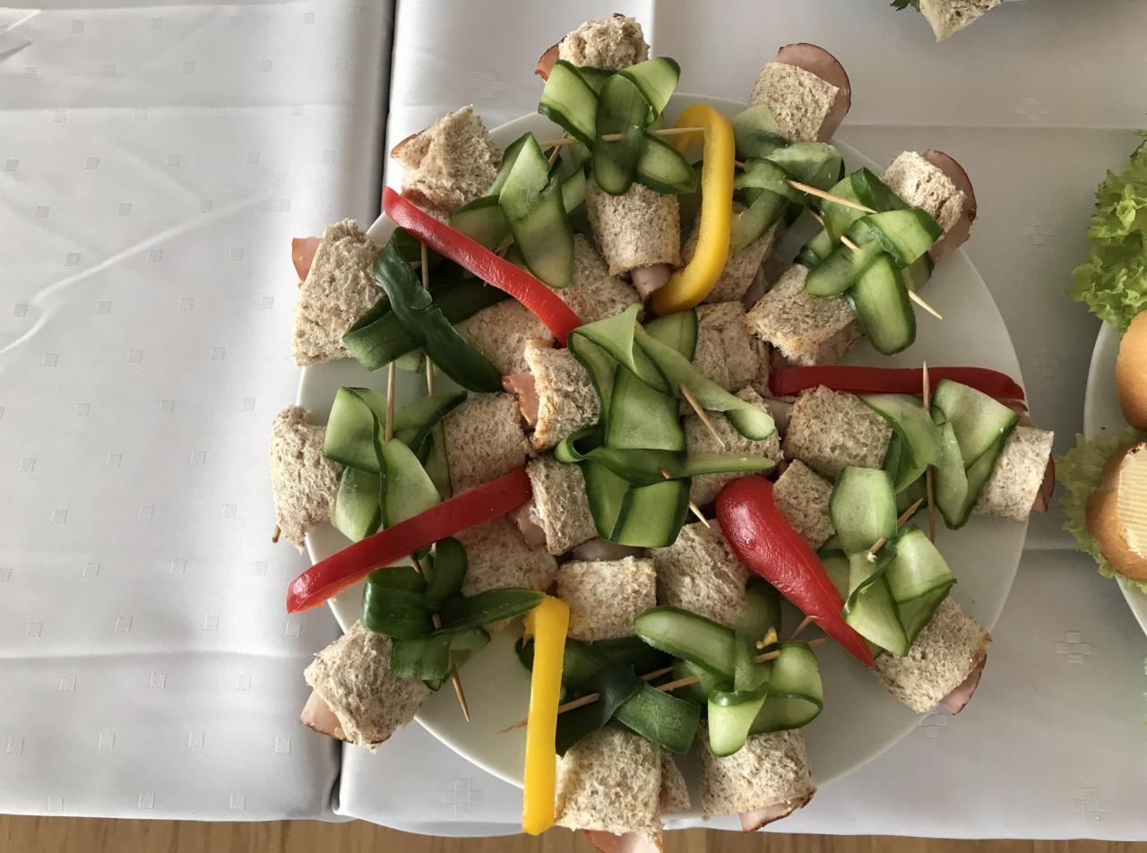 Dekoracyjnie podane mini kanapki z szynką i ogórkiem, ozdobione papryką na białym talerzu, widoczne z góry.