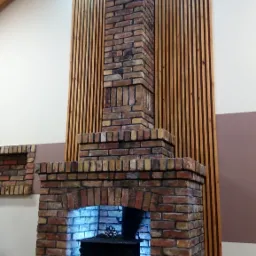 Murowany kominek z cegły w stylu rustykalnym z czarnym piecem w środku, oświetlony niebieskim światłem, na tle drewnianej boazerii i sufitu w Luzinie.