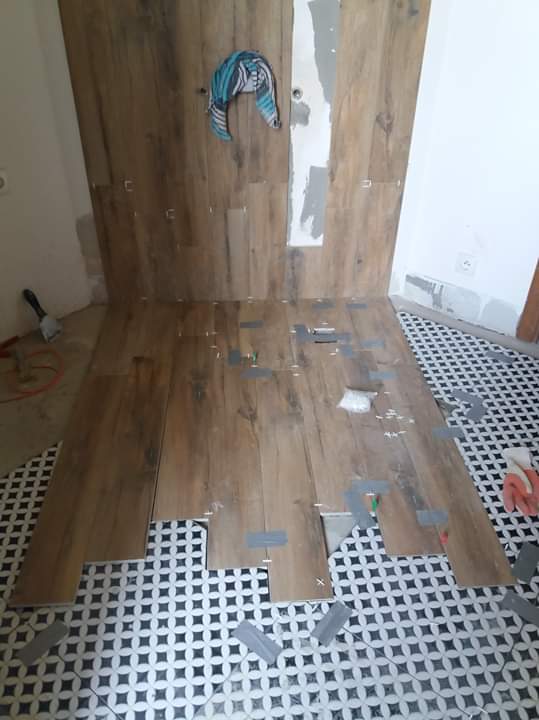 Montaż płytek imitujących drewno na podłodze w łazience, widoczne fragmenty podłogi z płytek w czarno-biały wzór, ślady kleju i poziomica na ścianie, ręcznik powieszony na ścianie.