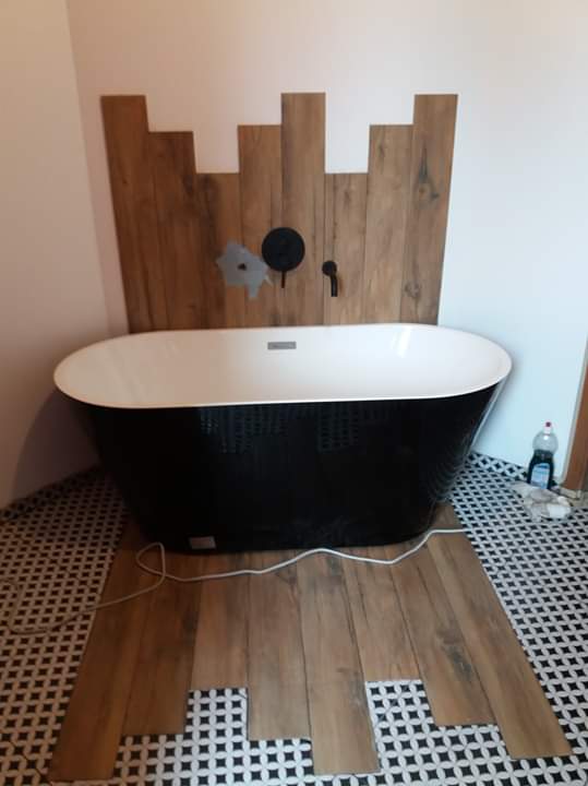 Czarno-biała wolnostojąca wanna na tle drewnianej mozaiki ściennej i podłogi w trakcie układania płytek.