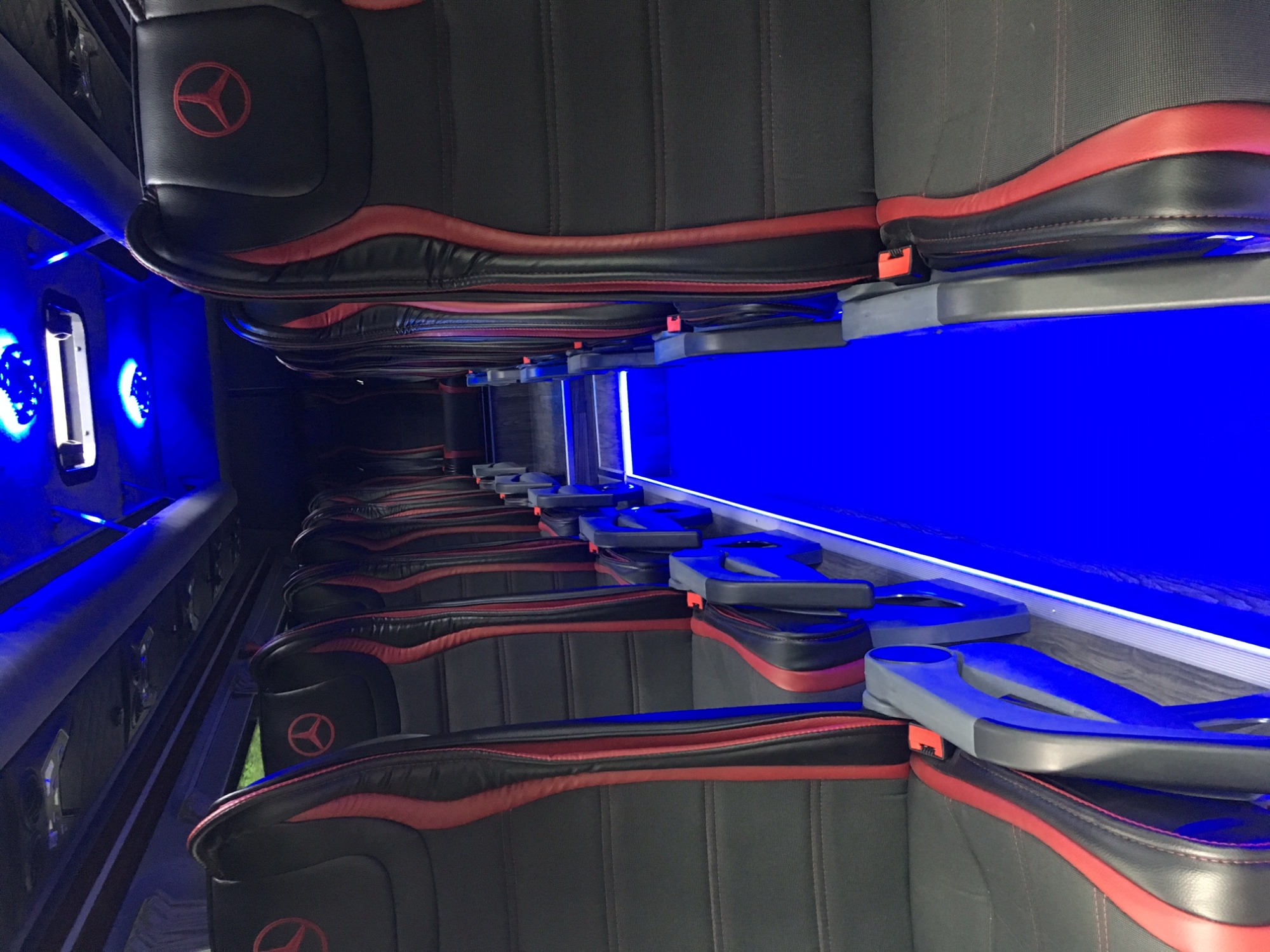 Wnętrze luksusowego busa Mercedes Sprinter z czarno-czerwonymi skórzanymi fotelami, podświetleniem LED i uchwytami na napoje.