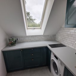 Smart Instal - Nowoczesna kuchnia na poddaszu z ciemnozielonymi szafkami, szarą płytą i oknem dachowym. Widoczna płyta indukcyjna i ekspres do kawy.