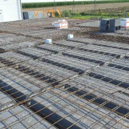 Zbrojenie stropu Teriva z pustakami betonowymi, widoczne elementy podpierające i otoczenie budowy.