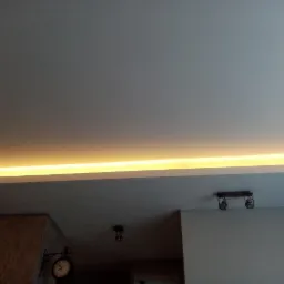 Sufit podwieszany z ukrytym oświetleniem LED, widoczne lampy punktowe i fragment ściany z zegarem.