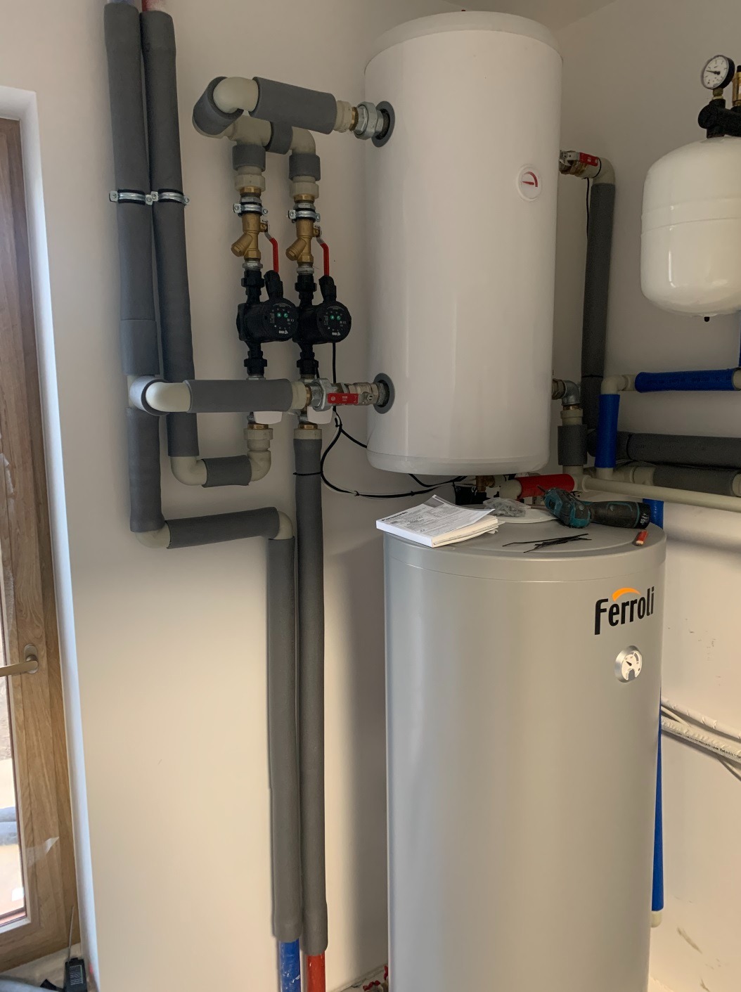 Instalacja z dwoma zbiornikami, orurowaniem w izolacji, pompami obiegowymi i narzędziami na zbiorniku Ferroli, widok podczas montażu.