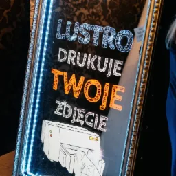 Podświetlane lustro z napisem 'Lustro drukuje Twoje zdjęcie' i rysunkiem drukarki, otoczone dekoracyjną ramą z niebieskim oświetleniem LED.