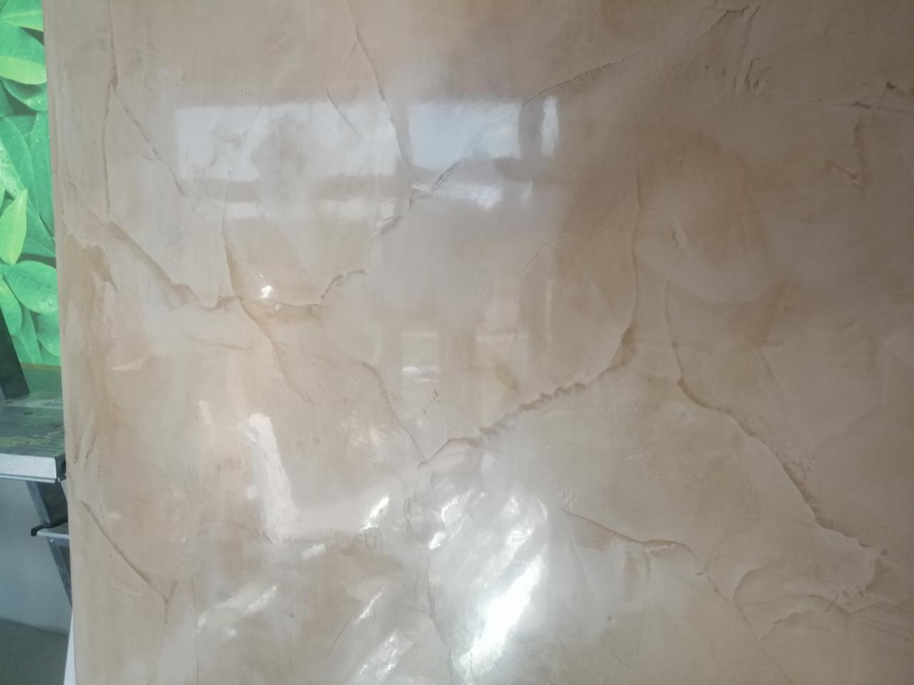 Beżowa ściana z dekoracyjną fakturą przypominającą marmur, z widocznym odbiciem światła.