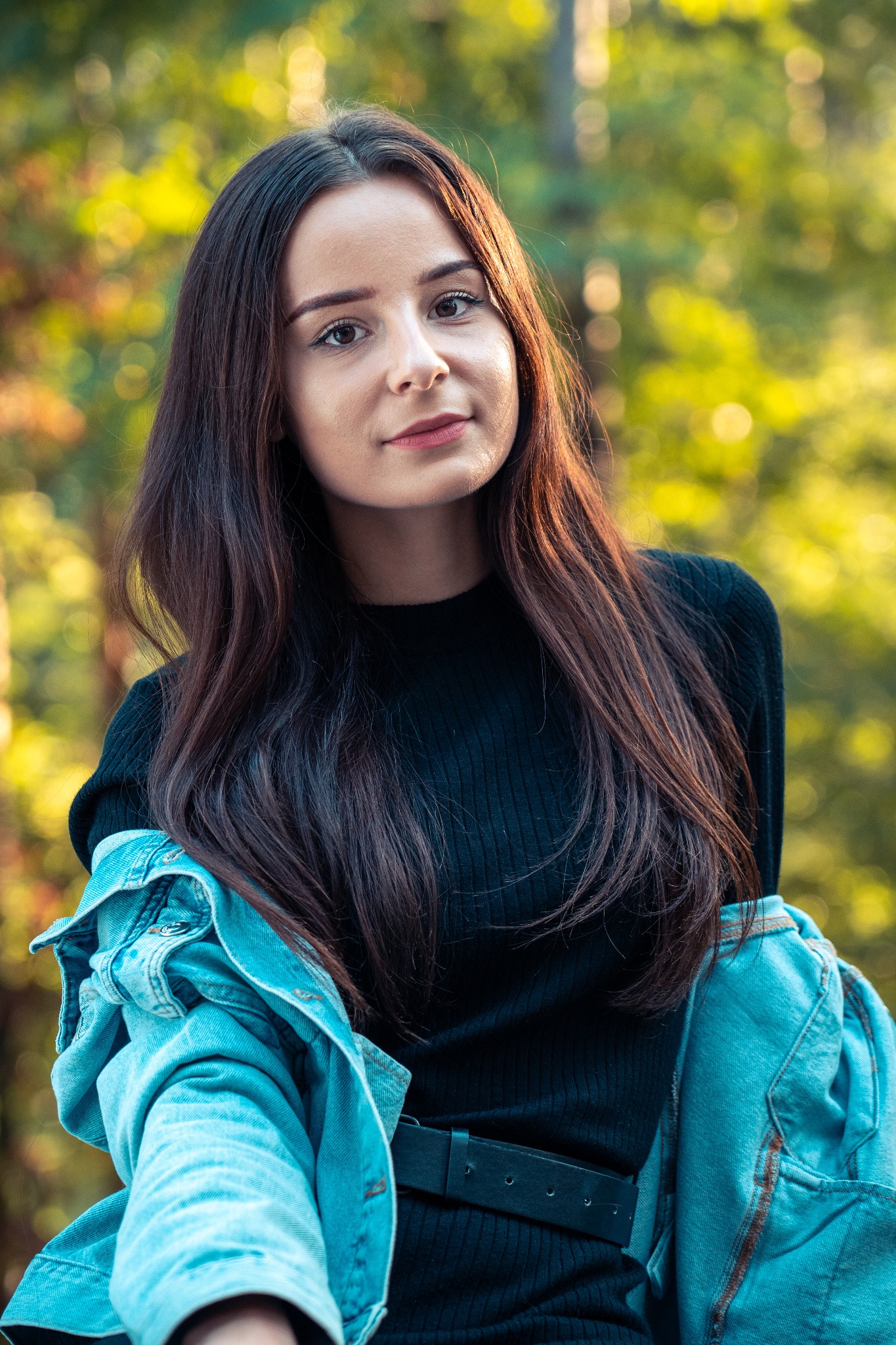 Portret młodej kobiety w czarnej bluzce i jeansowej kurtce na tle zieleni w Mielcu, wykonany w naturalnym świetle.