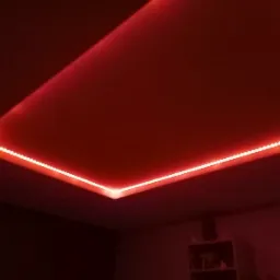 Czerwone oświetlenie LED wzdłuż krawędzi podwieszanego sufitu tworzące nowoczesny efekt wizualny w pomieszczeniu.