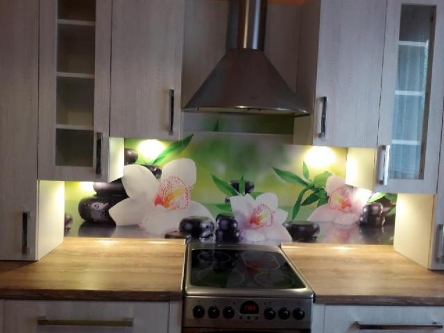 Nowoczesna kuchnia z jasnymi szafkami, drewnianym blatem i panelem dekoracyjnym z motywem orchidei i kamieni zen nad płytą grzewczą, oświetlona punktowo.