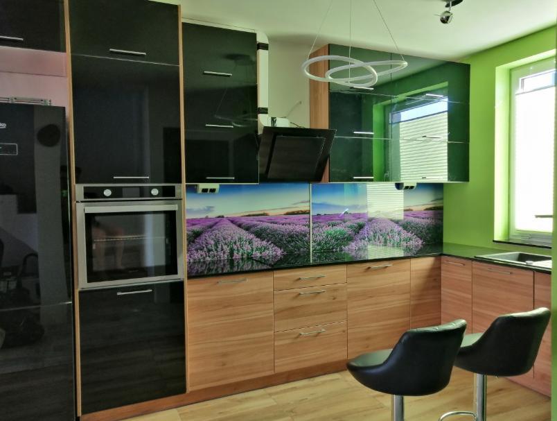 Nowoczesna kuchnia z czarnymi i drewnianymi frontami, podświetlanym panelem nad blatem z motywem lawendy, oraz dwoma czarnymi hokerami.