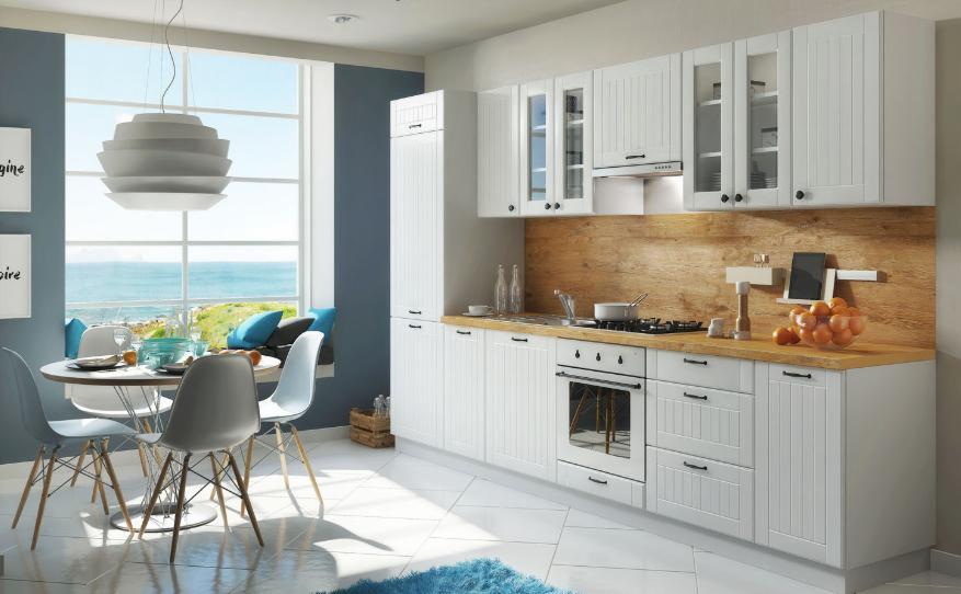 Jasna kuchnia w stylu skandynawskim z białymi frontami, drewnianym blatem i okrągłym stołem z widokiem na morze.