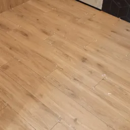 Układanie podłogi z płytek imitujących drewno, widoczne krzyżyki dystansowe, ściany wykończone różnymi rodzajami płytek.