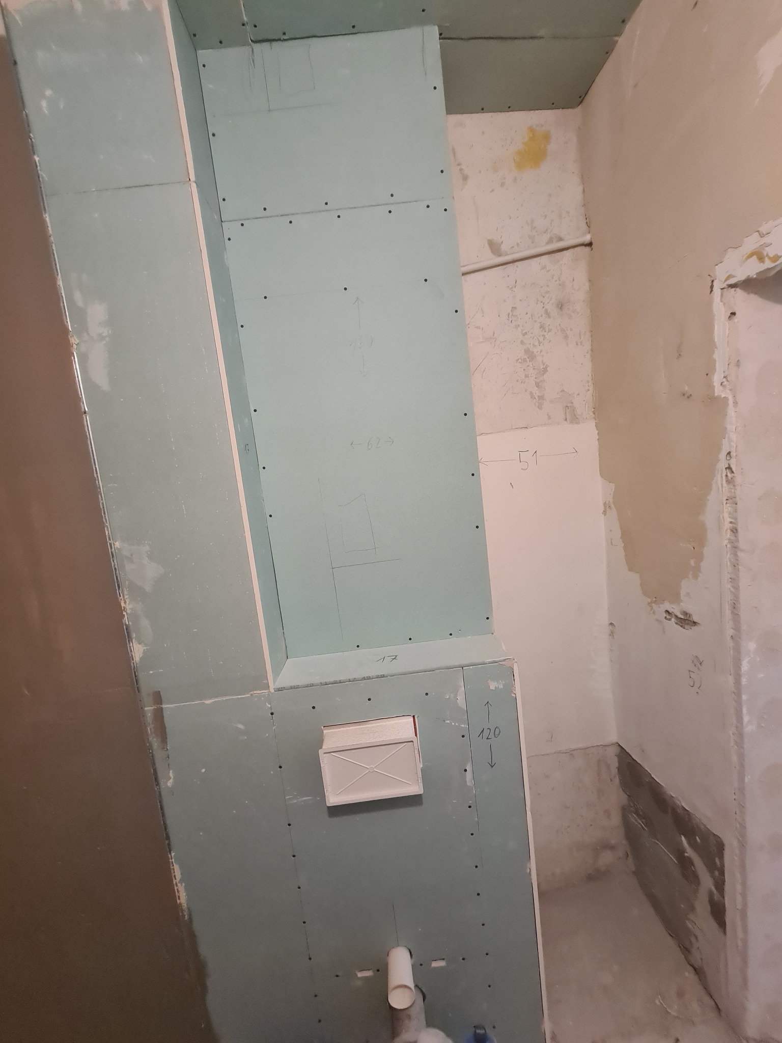 Surowy stan łazienki w Markach, z widocznymi płytami gipsowo-kartonowymi na ścianach, przygotowanymi do dalszych prac wykończeniowych. Na ścianach widoczne odręczne notatki z wymiarami.
