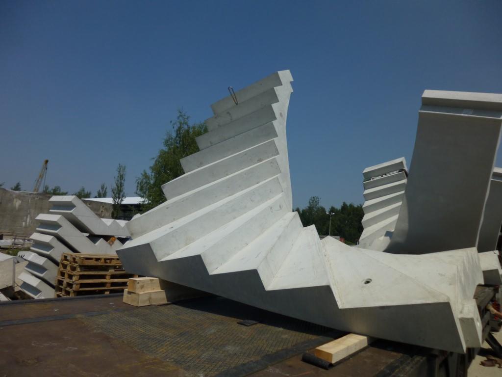 Prefabrykowane elementy betonowe schodów ułożone na pace samochodu ciężarowego, widoczny dźwig w tle.