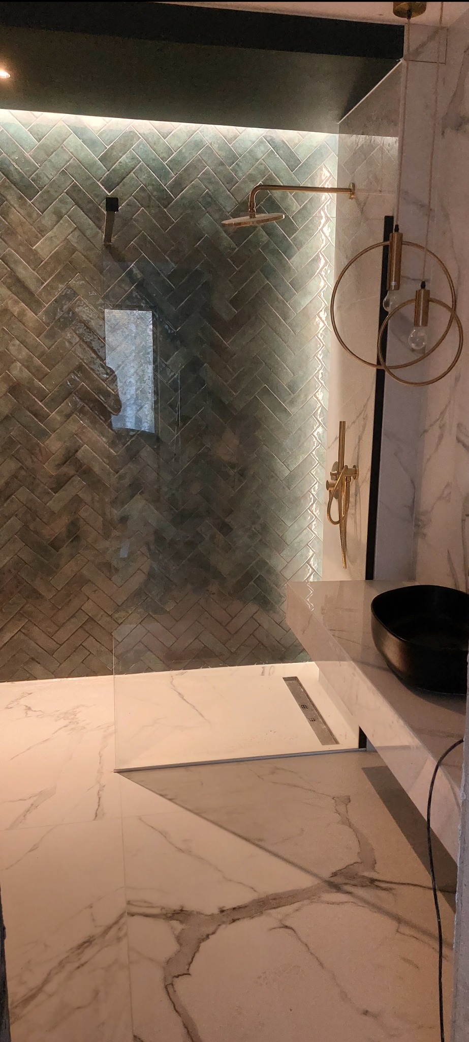 Nowoczesna kabina prysznicowa z zieloną, ułożoną w jodełkę glazurą w Warszawie, złota armatura i marmurowe płytki podłogowe.