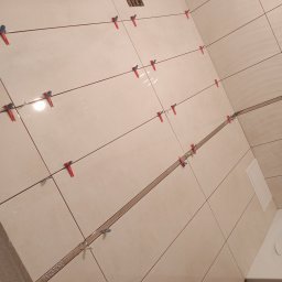 OdRemontuj - Ściana łazienki w Radomiu w trakcie układania płytek ceramicznych, z widocznymi krzyżykami dystansowymi i systemem poziomowania płytek.