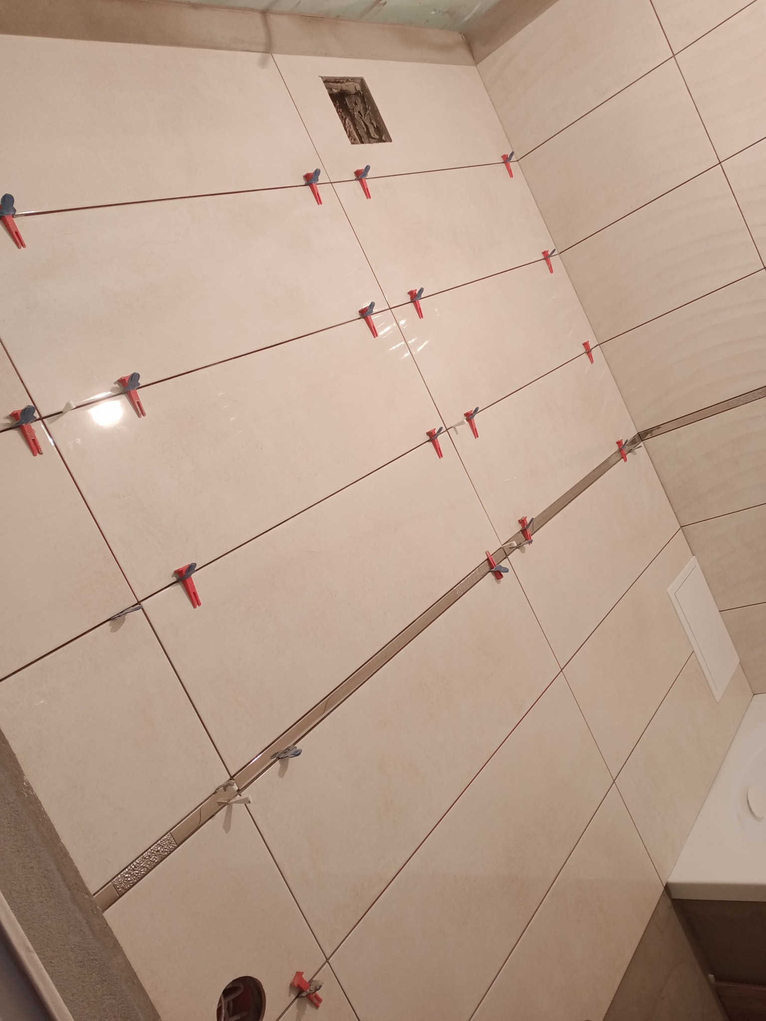 Ściana łazienki w Radomiu w trakcie układania płytek ceramicznych, z widocznymi krzyżykami dystansowymi i systemem poziomowania płytek.