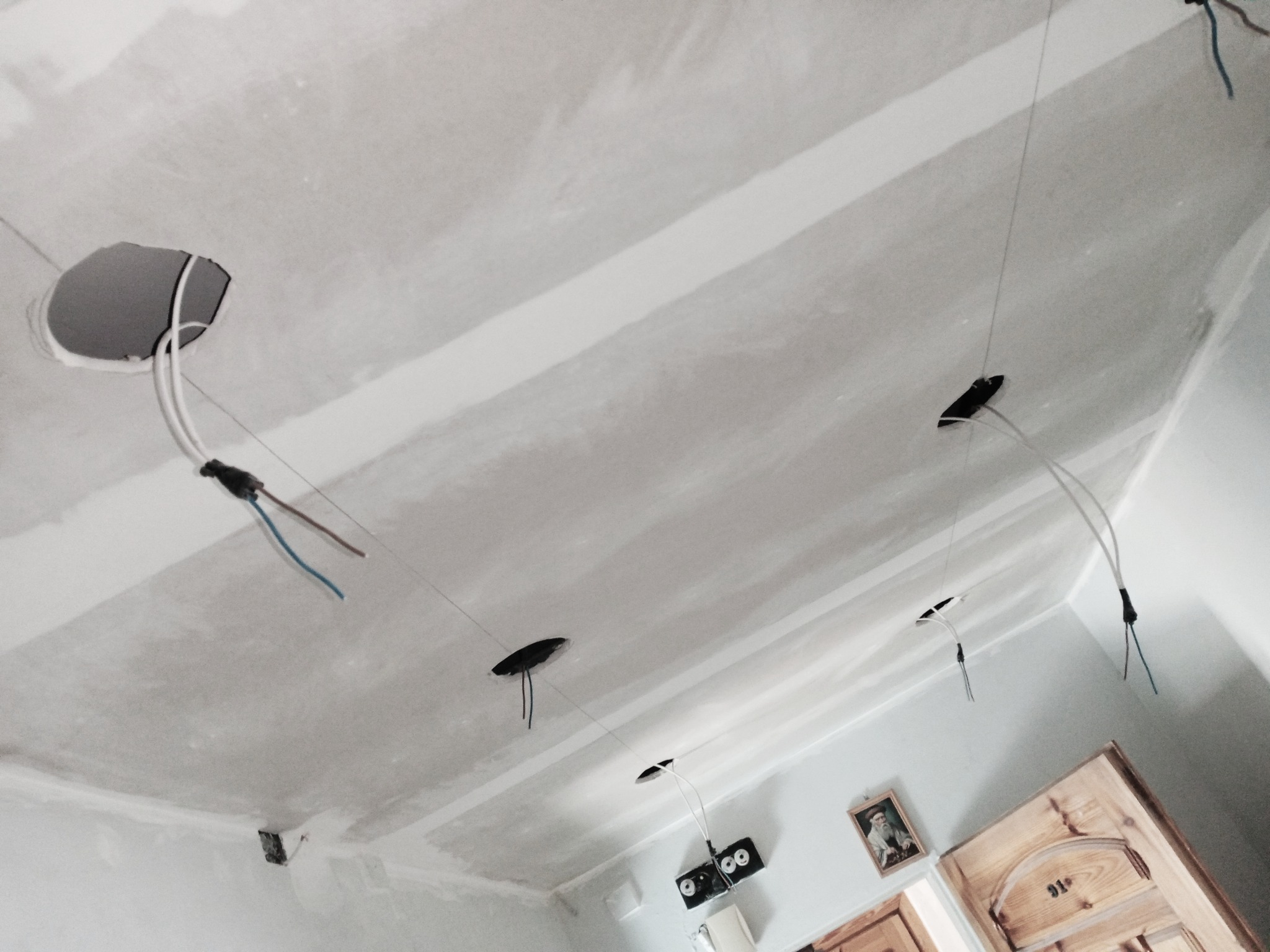 Sufit podwieszany w trakcie montażu z widocznymi otworami na oświetlenie i wystającymi przewodami elektrycznymi, szpachlowane łączenia płyt gipsowo-kartonowych.