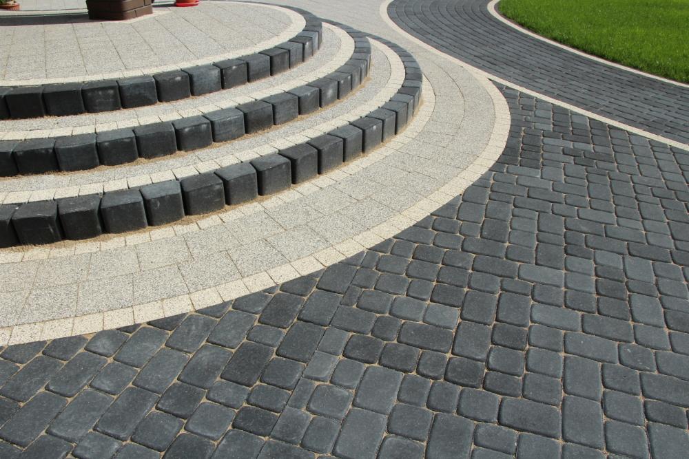 Kaskadowe schody z kostki brukowej w odcieniach szarości i czerni, obrzeża z jasnej kostki, widok z góry na fragment ścieżki.