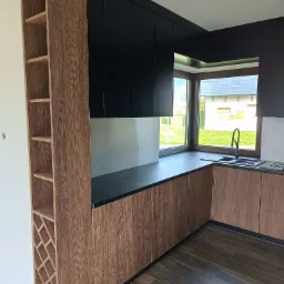 Nowoczesna kuchnia z zabudową na wymiar: czarne szafki górne i drewnopodobne szafki dolne, czarny blat, półka na wino z wzorem rombów.