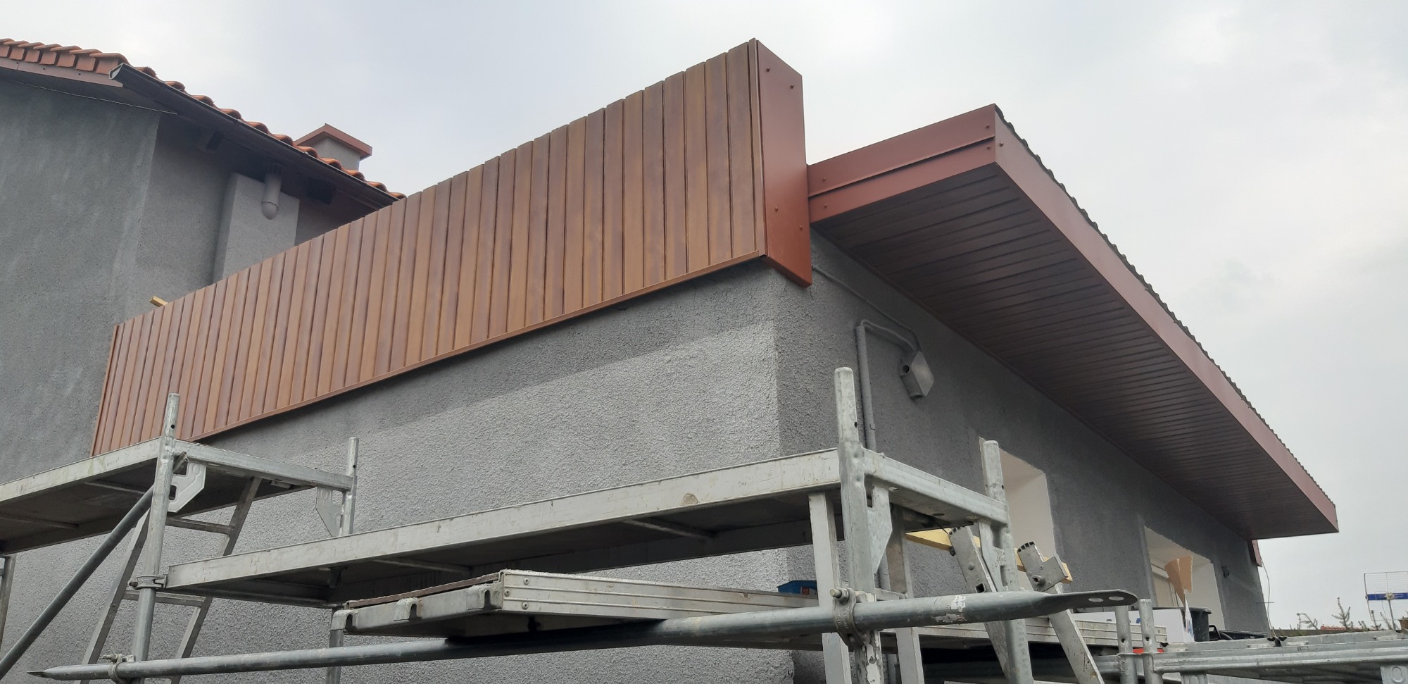 Wykończenie elewacji budynku z zastosowaniem paneli drewnopodobnych i obróbek blacharskich, widoczne rusztowanie.