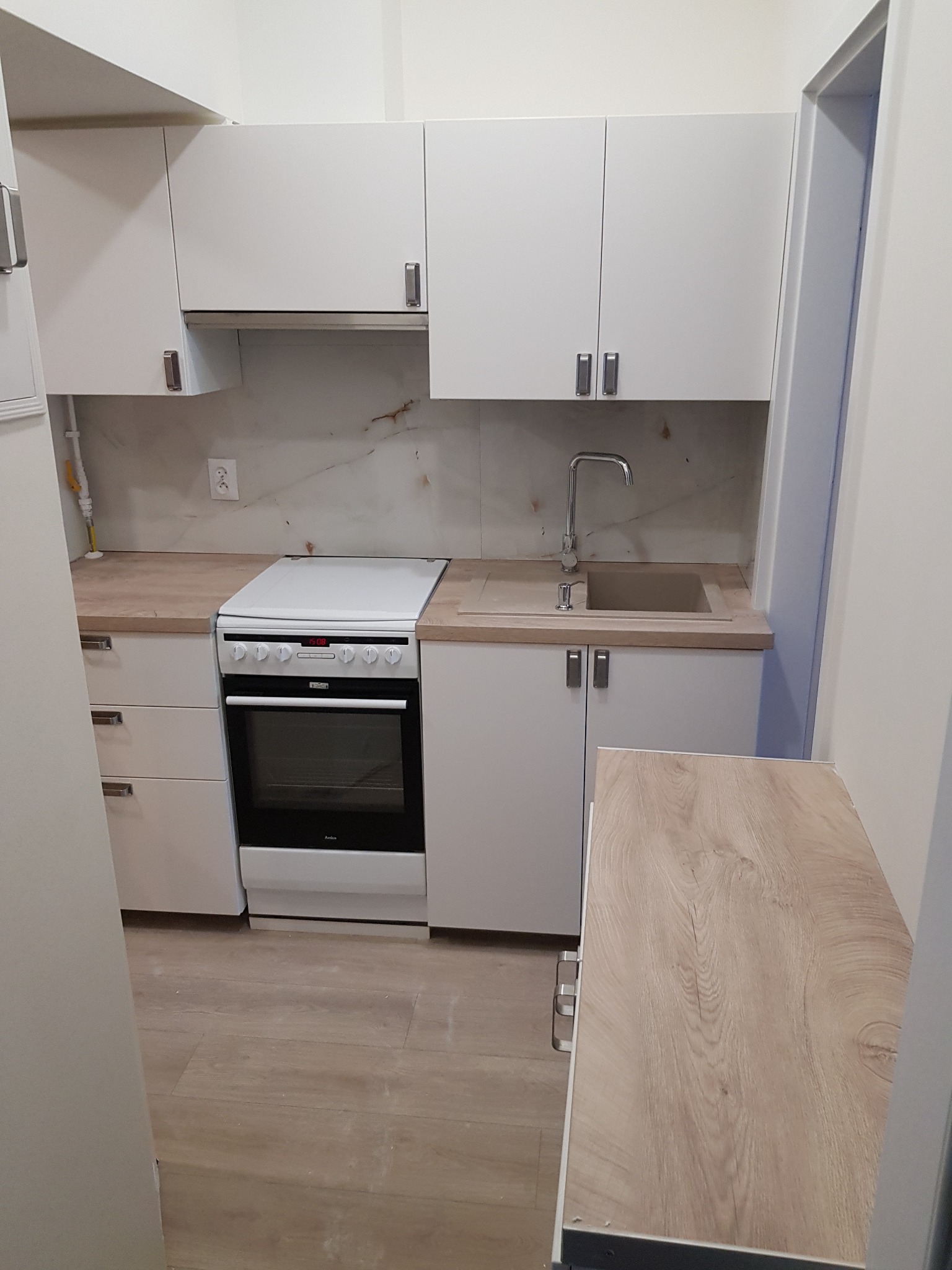 Jasna kuchnia w Wysokim Kościele z białymi szafkami, drewnianym blatem i płytą grzewczą Amica, widok z perspektywy wejścia do pomieszczenia.