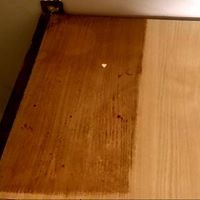 Fragment drewnianej powierzchni mebla przed i po czyszczeniu, widoczna wyraźna różnica w kolorze i czystości, zarys krawędzi mebla w lewym górnym rogu.