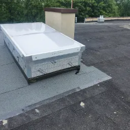 Świetlik dachowy z widocznym napisem 'ŚWIETO CHŁOWICE' na obudowie, zamontowany na dachu pokrytym papą, z kominem w tle.