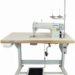 Profesjonalna maszyna do szycia JUKI z metalową stopką, pedałem nożnym i miarką na blacie roboczym, ustawiona na białym tle.