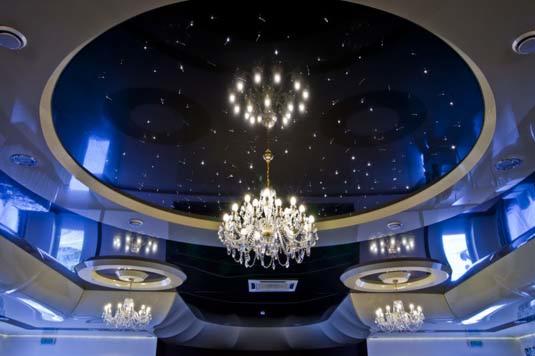 Okrągły, podwieszany sufit w kolorze ciemnoniebieskim z efektem gwiazd, oświetlony kryształowym żyrandolem, dodatkowo oświetlenie punktowe w suficie i ścianach.