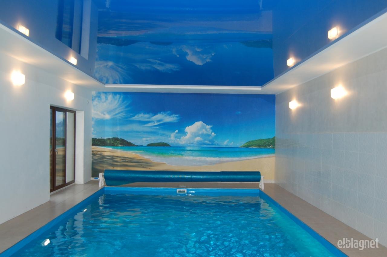 Kryty basen z fototapetą plaży na ścianie i suficie, oświetlenie punktowe.