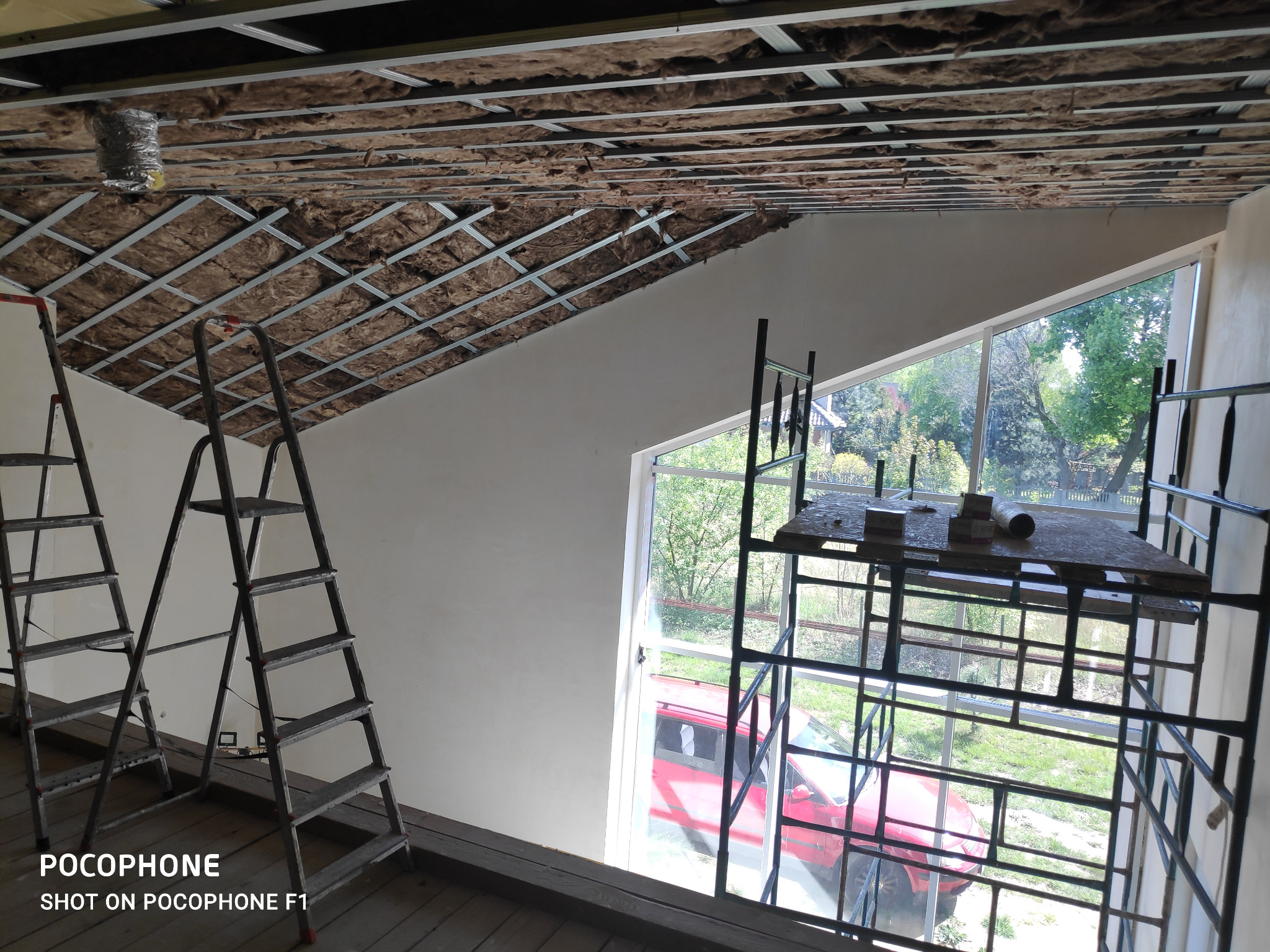 Montaż izolacji wełną mineralną w metalowym stelażu sufitu podwieszanego, widoczne drabiny i rusztowanie przy oknie.