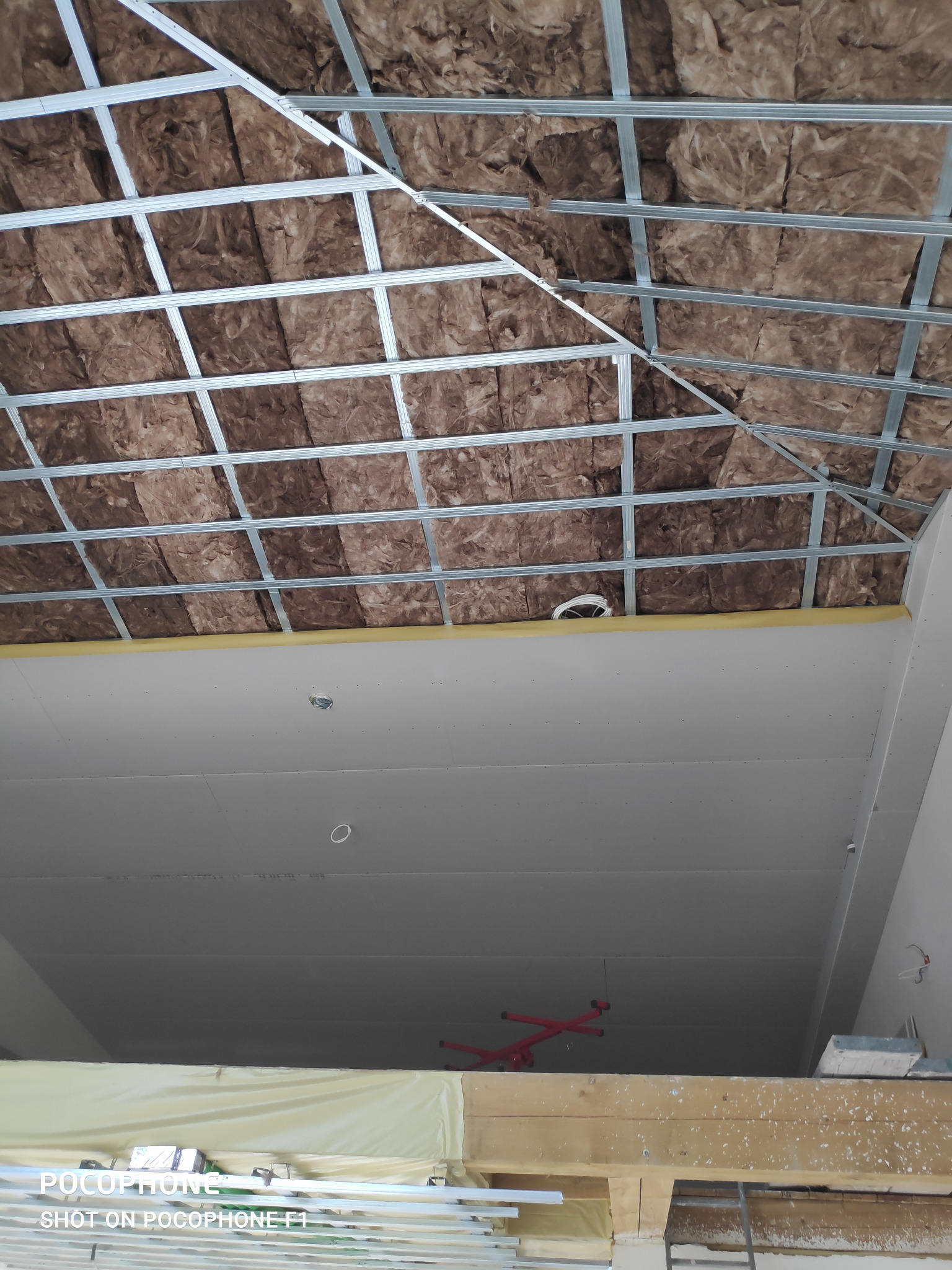 Montaż izolacji z wełny mineralnej w metalowym stelażu pod płytami gipsowo-kartonowymi na poddaszu, widok z dołu.