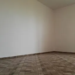 Pusta, jasna przestrzeń z beżowymi płytkami imitującymi kamień, ułożonymi w prostokątnym wzorze, widok z dołu na białe ściany.